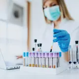 Wissenschaftlerin mit Maske und Handschuhen arbeitet mit Blutproben. Loreal tierversuche sind ein Thema, das hier nicht direkt gezeigt wird, aber die Forschung ist wichtig.