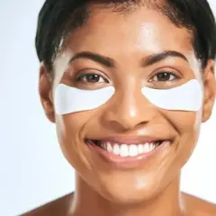 Lächelnde Frau mit weißen Augenpads. Ob morgens oder abends, sie erfrischen die Haut.