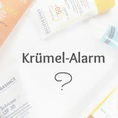Sonnencremes und ein Moisturizer liegen auf weißem Untergrund. Ein Fragezeichen und der Text "Krümel-Alarm" sind in der Mitte zu sehen.