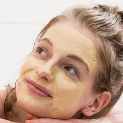 Frau mit Gesichtsmaske, die entspannt in die Ferne blickt. Tolle hautpflege tipps für strahlende Haut.
