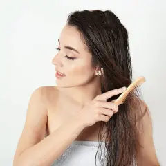 Junge Frau kämmt nasses Haar mit einem Holzkamm. Sie achtet auf ihre Spitzen, um abgebrochene Haare zu vermeiden.