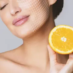 Frau mit Gitterlinien im Gesicht hält eine Orangenhälfte. Vitamin C gegen Pickel für strahlende Haut.