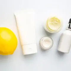 Kosmetikprodukte mit Zitrone, die an Retinol und Vitamin C erinnert, neben grünen Blättern.