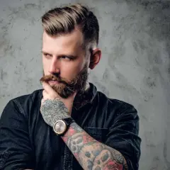 Ein Mann mit Bart und Tattoos, dessen Frisur mit Pomade gestylt ist. Er denkt nach, was ist Pomade?