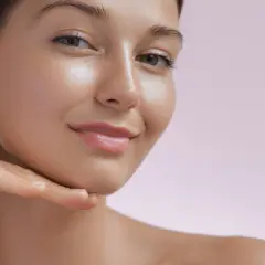Ein strahlendes Lächeln mit einem gesunden Glow im Gesicht. Eine Hand berührt sanft das Kinn.