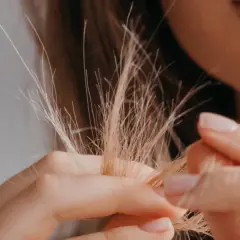 Nahaufnahme von blondem Haar, das sich in den Fingern verheddert. Die feinen, abstehenden Härchen zeigen, wie sieht Frizz aus.