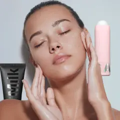 Ein Model mit geschlossenen Augen und feuchter Haut, umgeben von Milk Make-up Produkten. Was ist ein Primer? Er bereitet die Haut auf Make-up vor.