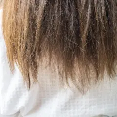 Langes, braunes Haar fällt über ein weißes Kleid. Die Spitzen sind etwas trocken, aber insgesamt sieht es nach gesunden Haaren aus.
