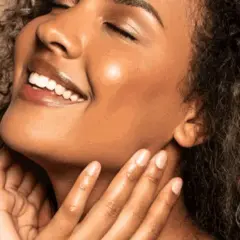 Strahlendes Lächeln einer Frau mit lockigem Haar. Ihre Haut wirkt frisch und glatt, ein Zeichen für gute Pflege und regelmäßige Exfoliation.