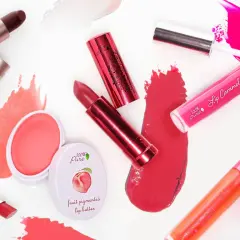 Verschiedene Lippenstifte und Lipglosse in Rottönen und Pink. Die Produkte bestehen aus natürlichen Inhaltsstoffen, wie Fruchtpigmenten.