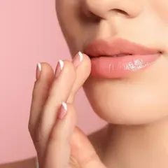 Nahaufnahme von Lippen, die gerade Lipgloss auftragen. Die Finger mit französischem Maniküre-Nageldesign berühren sanft die Lippen.