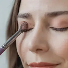 Eine Frau trägt mit einem Pinsel sanft Lidschatten auf. So gelingt das lidschatten richtig auftragen für einen strahlenden Blick.
