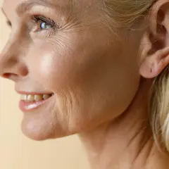 Profil einer lächelnden Frau mit sichtbaren Lachfalten um Mund und Augen. Ihr blondes Haar umrahmt ihr Gesicht.
