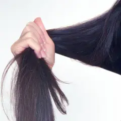 Frau mit dunklem Haar, das sie in der Hand hält. Tipps für trockene Haare, was tun?