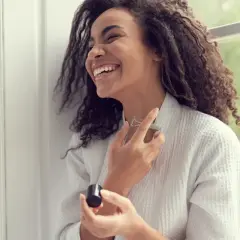 Frau lacht und sprüht sich Parfum auf den Hals. Reine Kosmetik ohne Konservierungsstoffe für ein frisches Gefühl.