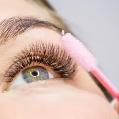 Ein rosa Bürstchen wird sanft über voluminöse Wimpern geführt, um die **Wimpern pflegen** und perfekt zu stylen.