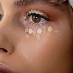 Kleine Tupfer von hellem Concealer unter dem Auge, um zu zeigen, was ein Concealer ist und wie er kleine Makel abdeckt.