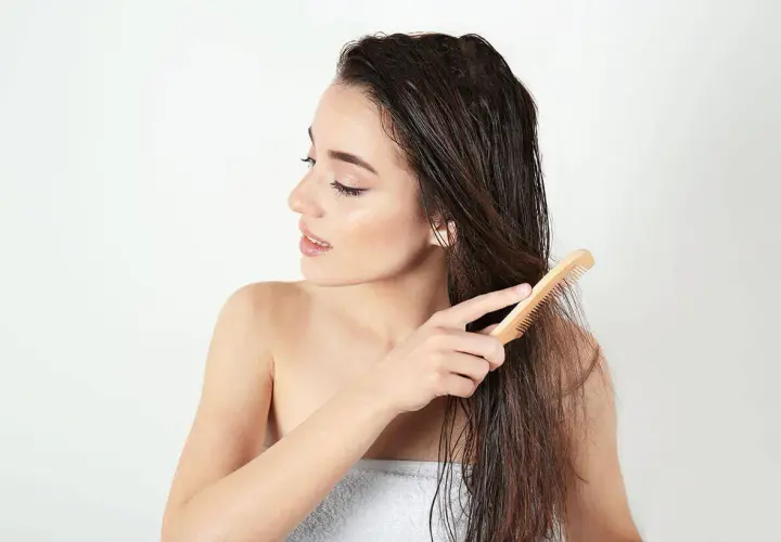 Junge Frau kämmt nasses Haar mit einem Holzkamm. Sie achtet auf ihre Spitzen, um abgebrochene Haare zu vermeiden.
