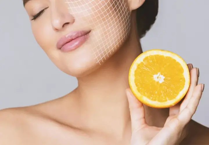 Frau mit Gitterlinien im Gesicht hält eine Orangenhälfte. Vitamin C gegen Pickel für strahlende Haut.