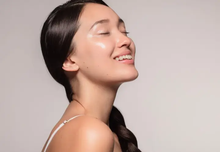 Ein lächelndes Gesicht mit strahlender, **glass skin**-ähnlicher Haut, die von Feuchtigkeit glänzt.