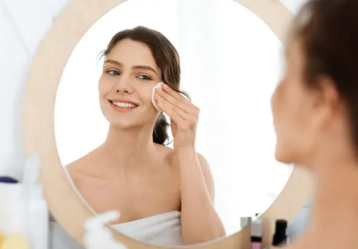 Lächelnde Frau reinigt ihr Gesicht mit einem Wattepad. Sie nutzt die Kraft von Retinol gegen Akne für reine Haut.