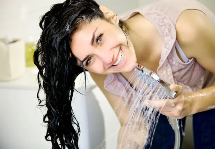 Frau mit nassem Haar lacht unter der Dusche. Sie fragt sich, was sind Silikone im Shampoo und wie sie das Haar glänzend machen.