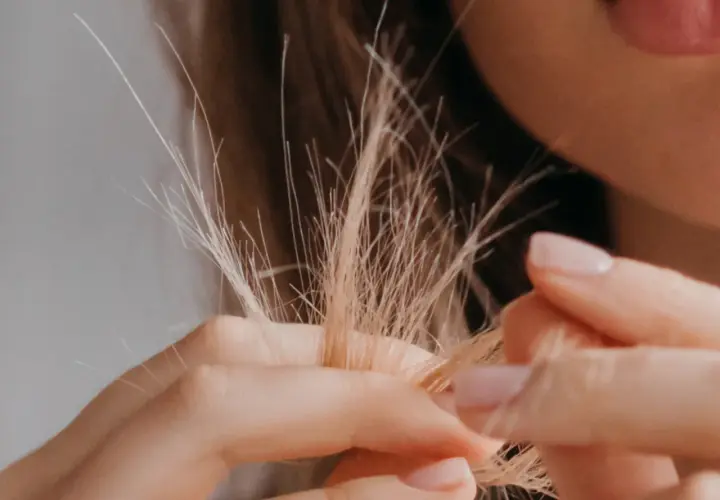 Nahaufnahme von blondem Haar, das sich in den Fingern verheddert. Die feinen, abstehenden Härchen zeigen, wie sieht Frizz aus.