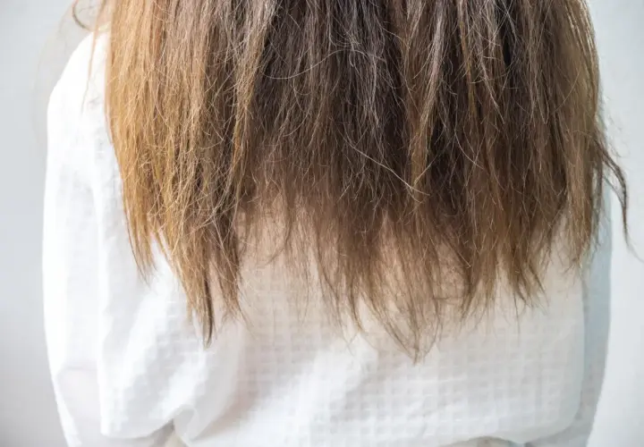 Langes, braunes Haar fällt über ein weißes Kleid. Die Spitzen sind etwas trocken, aber insgesamt sieht es nach gesunden Haaren aus.