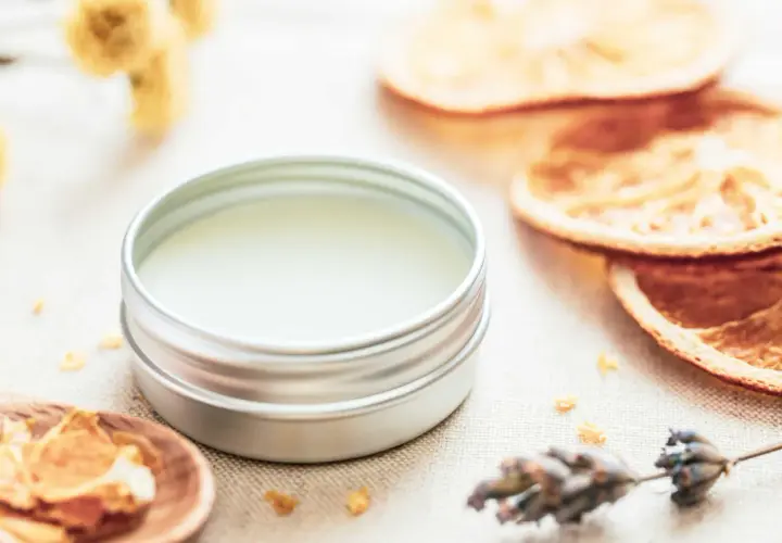 Ein Döschen mit selbstgemachtem Lippenbalsam, umgeben von getrockneten Orangen, Lavendel und Kräutern.