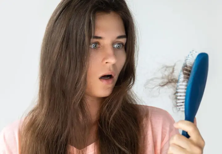 Schockiert blickt eine Frau auf ihre Haarbürste mit vielen ausgefallenen Haaren. Hoffentlich hilft Rosmarin Haare vorher nachher.