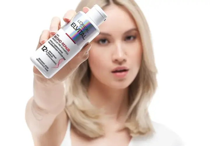 Frau hält L'Oréal Elvital Bond Repair Pre-Shampoo, das hilft, trockene Haare zu reparieren.