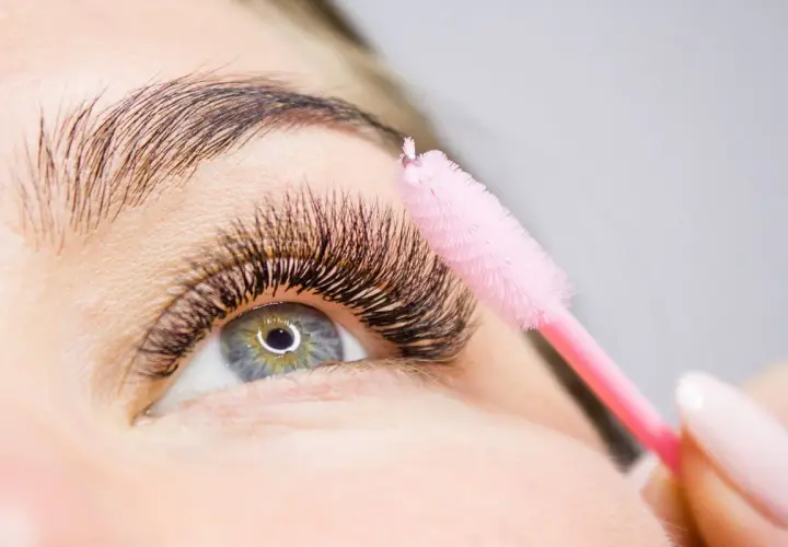 Ein rosa Bürstchen wird sanft über voluminöse Wimpern geführt, um die **Wimpern pflegen** und perfekt zu stylen.