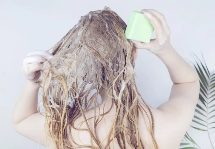 Frau wäscht sich die Haare mit einem grünen Stück biologisch abbaubares Shampoo.
