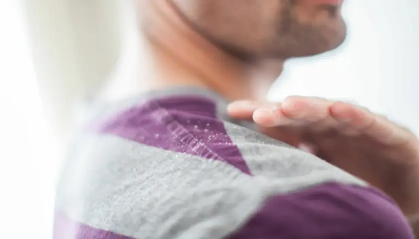 Schuppen auf dem Pullover. Vielleicht hilft Joghurt gegen Schuppen? Eine Hand wischt über die Schulter.