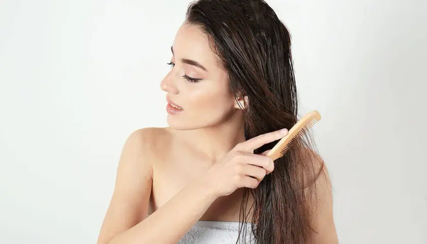 Junge Frau kämmt nasses Haar mit einem Holzkamm. Sie achtet auf ihre Spitzen, um abgebrochene Haare zu vermeiden.