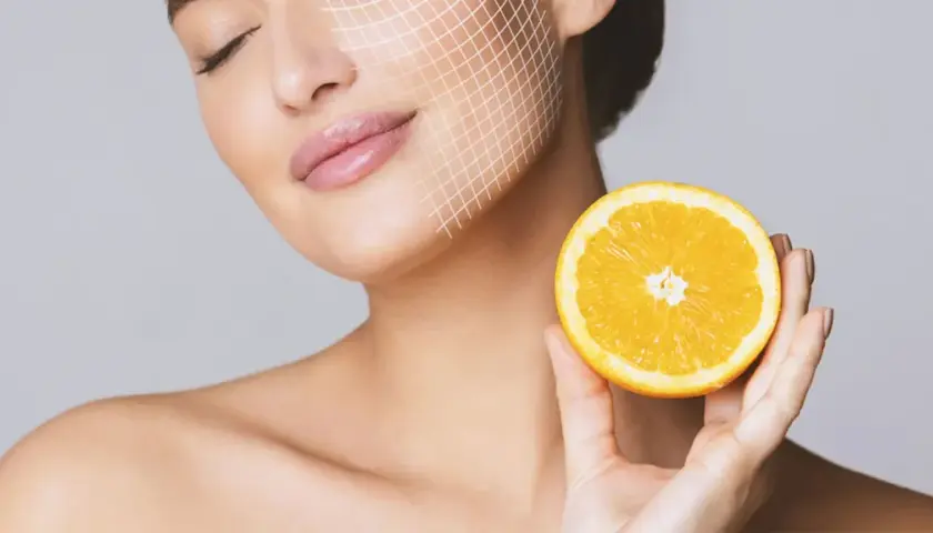 Frau mit Gitterlinien im Gesicht hält eine Orangenhälfte. Vitamin C gegen Pickel für strahlende Haut.