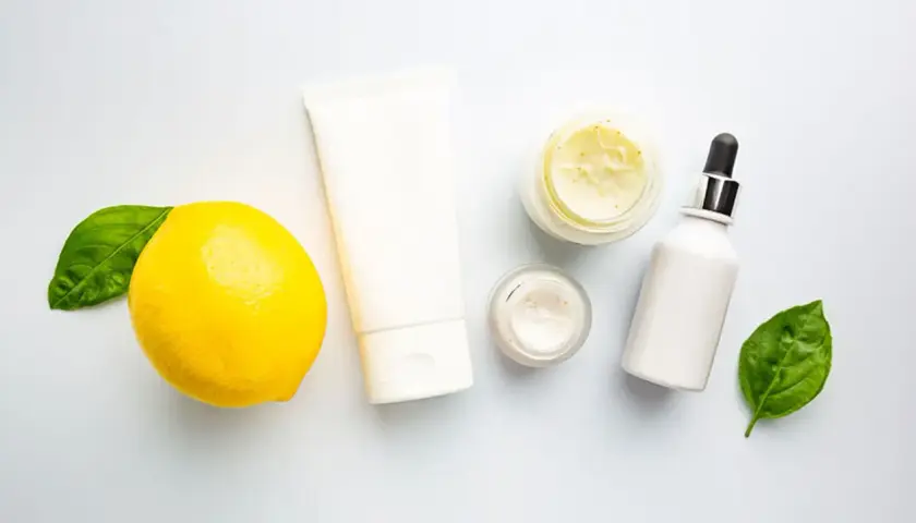 Kosmetikprodukte mit Zitrone, die an Retinol und Vitamin C erinnert, neben grünen Blättern.