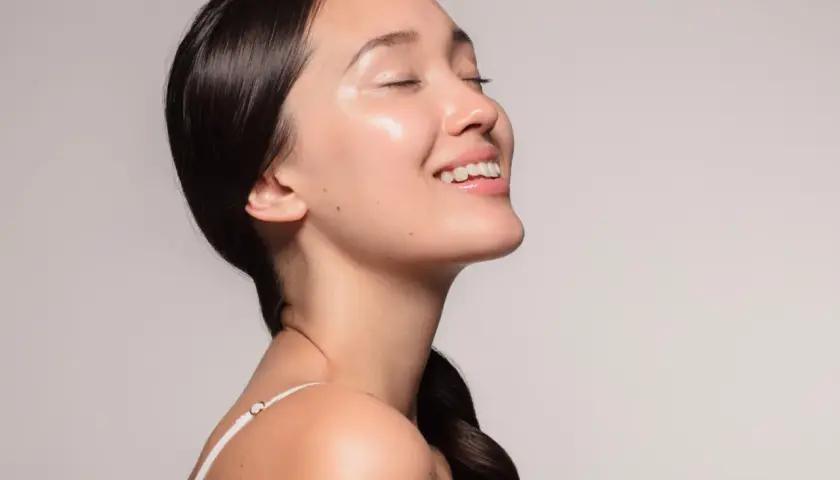 Ein lächelndes Gesicht mit strahlender, **glass skin**-ähnlicher Haut, die von Feuchtigkeit glänzt.