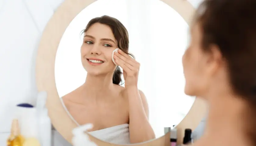 Lächelnde Frau reinigt ihr Gesicht mit einem Wattepad. Sie nutzt die Kraft von Retinol gegen Akne für reine Haut.