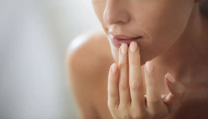 Frau trägt Lippenbalsam auf, um trockene Lippen zu behandeln. Sanfte Pflege für geschmeidige Lippen.