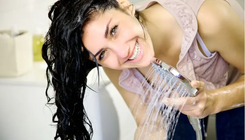 Frau mit nassem Haar lacht unter der Dusche. Sie fragt sich, was sind Silikone im Shampoo und wie sie das Haar glänzend machen.