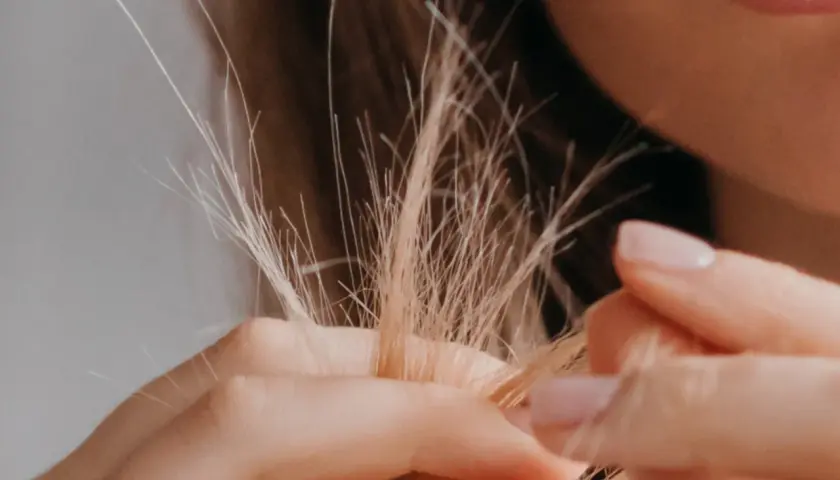 Nahaufnahme von blondem Haar, das sich in den Fingern verheddert. Die feinen, abstehenden Härchen zeigen, wie sieht Frizz aus.
