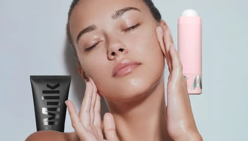 Ein Model mit geschlossenen Augen und feuchter Haut, umgeben von Milk Make-up Produkten. Was ist ein Primer? Er bereitet die Haut auf Make-up vor.