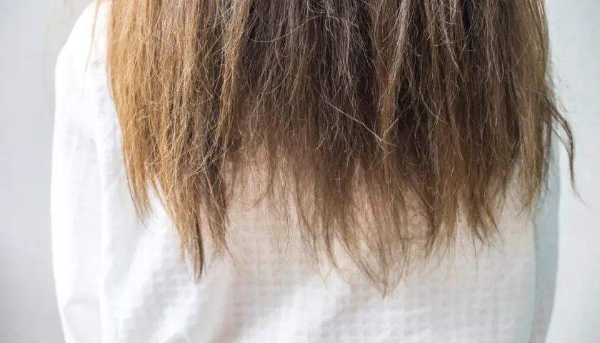 Langes, braunes Haar fällt über ein weißes Kleid. Die Spitzen sind etwas trocken, aber insgesamt sieht es nach gesunden Haaren aus.