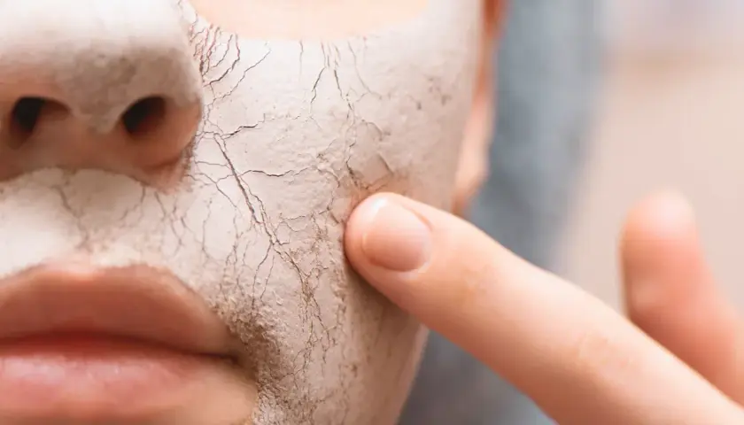 Nahaufnahme einer Maske auf dem Gesicht, die die sehr trockene Haut darunter zeigt. Ein Finger berührt die rissige Textur.
