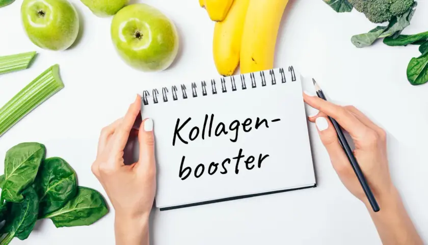 Grüne Äpfel, Bananen, Sellerie, Spinat und Brokkoli – Zutaten für kollagenhaltige Lebensmittel, die auf einem Notizbuch mit der Aufschrift "Kollagen-Booster" liegen.