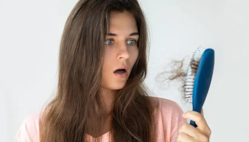 Schockiert blickt eine Frau auf ihre Haarbürste mit vielen ausgefallenen Haaren. Hoffentlich hilft Rosmarin Haare vorher nachher.