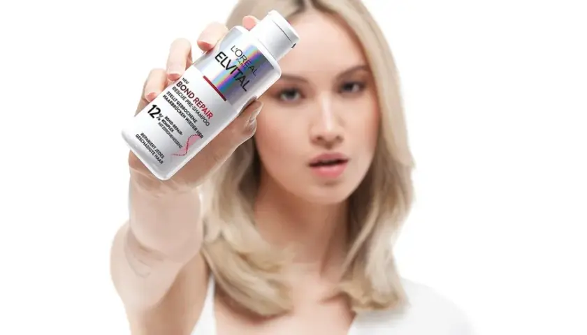 Frau hält L'Oréal Elvital Bond Repair Pre-Shampoo, das hilft, trockene Haare zu reparieren.
