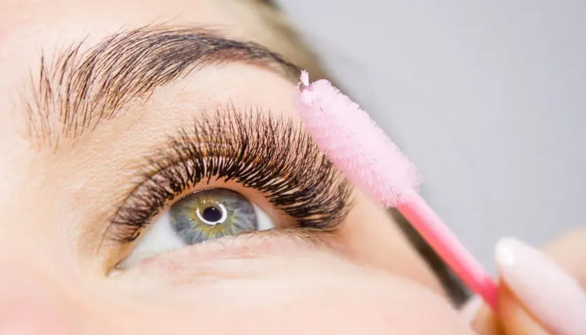 Ein rosa Bürstchen wird sanft über voluminöse Wimpern geführt, um die **Wimpern pflegen** und perfekt zu stylen.