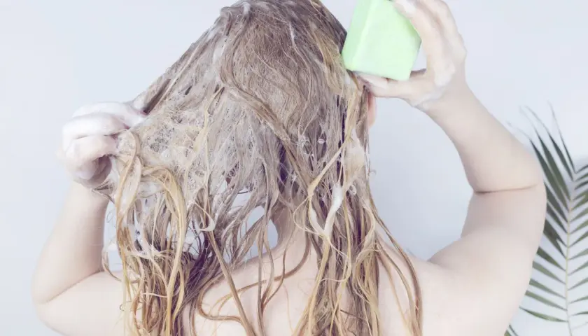 Frau wäscht sich die Haare mit einem grünen Stück biologisch abbaubares Shampoo.